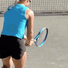 a woman in a blue tank top and black shorts is holding a tennis racket on a tennis court .