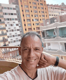 a man with his hand on his chin smiles in front of a balcony