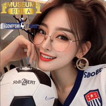 a woman wearing glasses holds a soccer ball in front of a museum bola logo