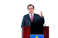 a man in a suit and tie is giving a speech at a podium with a flag on it