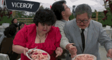 a woman in a red dress is holding a plate of food next to a man in a suit under a sign that says viceroy