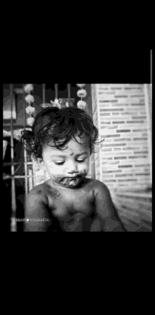 a black and white photo of a baby with cake on his face and a tattoo on his arm .