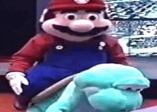 a mario mascot is riding on the back of a stuffed turtle .