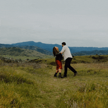 a man and a woman are dancing in a grassy field with mountains in the background