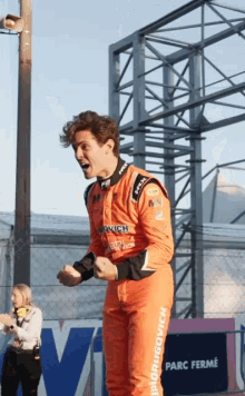 a man in an orange racing suit is standing in front of a sign that says " parc ferme "