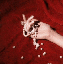 a woman 's hand is holding a string of pearls on a red cloth .