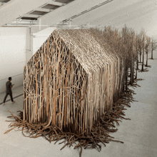 a man walks past a building made of sticks