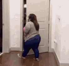 a woman in a gray shirt and blue jeans is walking through a door .