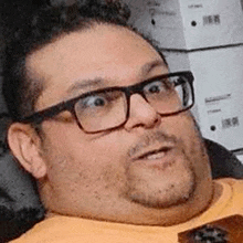 a man with glasses and a beard is sitting in a chair with boxes in the background .