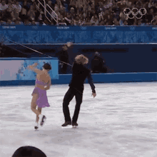 a man and a woman are ice skating in front of a sign that says ' olympics ' on it