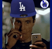 a man wearing a blue dodgers hat looks at his phone