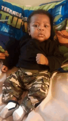 a baby is sitting on a bed with a teenage mutant ninja turtle pillow