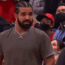 a man with a beard and braids is sitting in the stands at a basketball game and touching his hair .