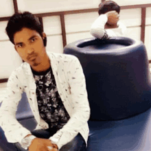 a man in a white jacket sits in front of a blue cylinder