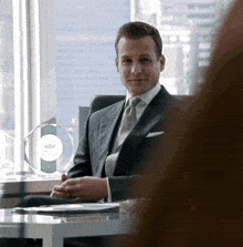 a man in a suit and tie sits at a desk in front of a glass plaque with a crown on it