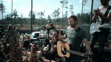 a man playing an acoustic guitar in front of a crowd with a man playing a bass guitar behind him