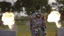 a man in a colorful shirt is standing in front of a cemetery with flames coming out of it .