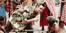 a man in a hawaiian shirt is kneeling down in front of a group of people and talking to them .