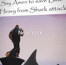 a statue of a man standing in front of a shark says amen to save new york