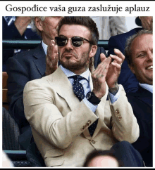 a man in a suit and tie applauds while wearing sunglasses and a watch