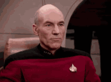 a bald man wearing a red and black uniform with a star trek badge