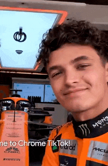 a young man with curly hair is taking a selfie in front of a race car in a garage .