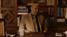 a man sits at a desk in front of a bookshelf with a mug that says " i 'm a scientist "