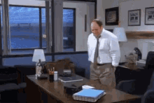 a man in a white shirt and tie is standing in front of a desk with binders on it .