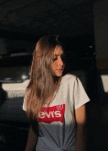 a girl wearing a levis t-shirt is standing in front of a car .