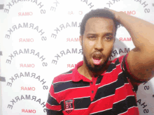 a man in a red and black striped shirt is standing in front of a wall that says " ehjaamaah "