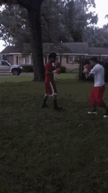 a man in a white shirt with the letter t on it is boxing with another man in red shorts