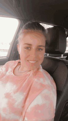 a woman in a pink tie dye shirt is smiling while sitting in a car