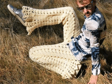 a man wearing crocheted pants and a tie dye shirt is kneeling in the grass