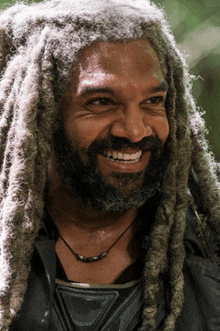 a man with dreadlocks and a beard smiles at the camera