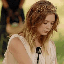 a woman wearing a crown on her head and a white dress is sitting in the grass .