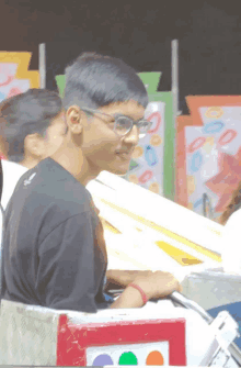 a boy wearing glasses and a black shirt is riding a carnival ride