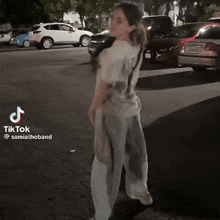 a woman in a tie dye shirt is standing in front of a parking lot with cars parked on the side of the road