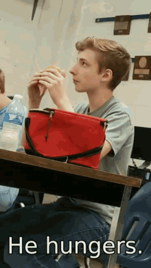 a young man sits at a desk with a red lunch bag on his lap and the words he hungers below him