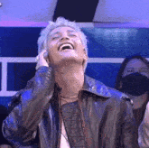 a man in a leather jacket is laughing while holding his hand to his ear .