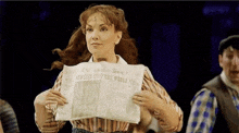 a woman in a striped shirt is holding a newspaper in her hands .