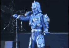 a blue superhero is singing into a microphone on stage .