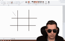 a man wearing sunglasses stands in front of a computer screen with a drawing of a cross