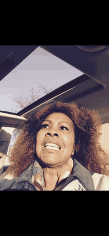 a woman with curly hair is smiling while sitting in a car with the sunroof open