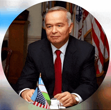 a man in a suit and tie sits at a table with an american flag