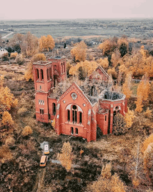 an aerial view of an old red brick church surrounded by yellow trees