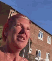 a woman with red hair is standing in front of a brick building with a blue sky in the background .