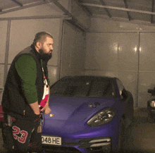 a man is standing in front of a purple car with a license plate that says 048 he