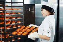 a woman is holding a tray of bread in front of a rack of bread and the word jij is on the bottom