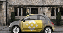 a gray car with a yellow and white logo on the side is parked in front of a stone building