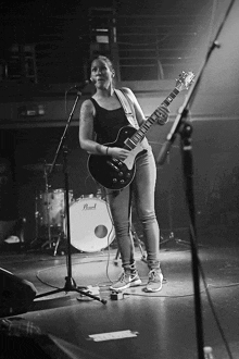 a woman playing a guitar and singing into a microphone on a stage with a pearl drum in the background